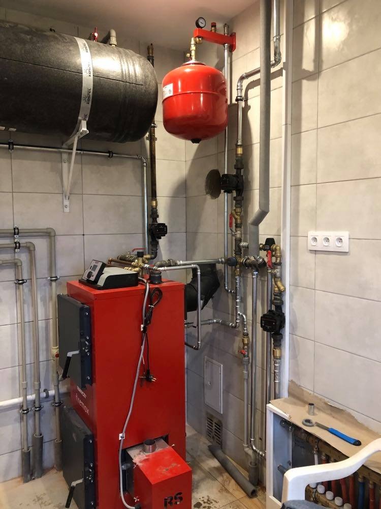 Czerwony piec grzewczy marki Firemax z czarnym zbiornikiem akumulacyjnym i czerwonym naczyniem wzbiorczym w kotłowni wyłożonej jasnymi płytkami.