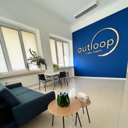 OUTLOOP Sp. z o.o. - Nowoczesne biuro firmy Outloop w Warszawie, z niebieską ścianą z dużym złotym logo 'TRUDNE KREDYTY', wygodną sofą, stolikami z wodą i stołem konsultacyjnym przy oknie.
