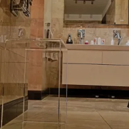 Nowoczesna łazienka z umywalką nablatową, lustrem i krzesłem o geometrycznej konstrukcji, wykończona płytkami w odcieniach beżu i brązu.