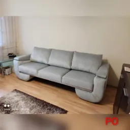 Szara, trzyosobowa sofa z niskim oparciem i metalową ramą, stojąca na drewnianej podłodze w pokoju z beżowymi ścianami i dywanem.