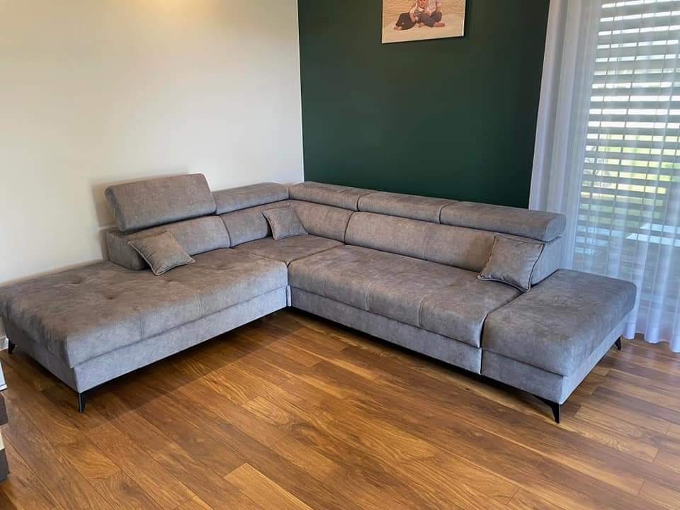 Szary narożnik tapicerowany z regulowanymi zagłówkami na drewnianej podłodze, widok z niskiej perspektywy.