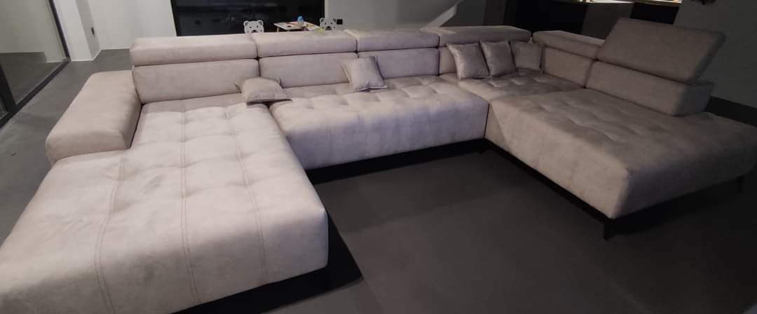 Jasnoszary, modułowy narożnik z regulowanymi zagłówkami i pikowanymi siedziskami, ustawiony w nowoczesnym wnętrzu.