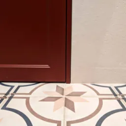 Fragment łazienki z bordową szafką i dekoracyjną, wzorzystą podłogą z płytek w stylu retro.