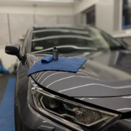 Błyszcząca maska auta z reflektorem, niebieska ściereczka z mikrofibry i butelka produktu do detailingu w studiu pielęgnacji pojazdów.