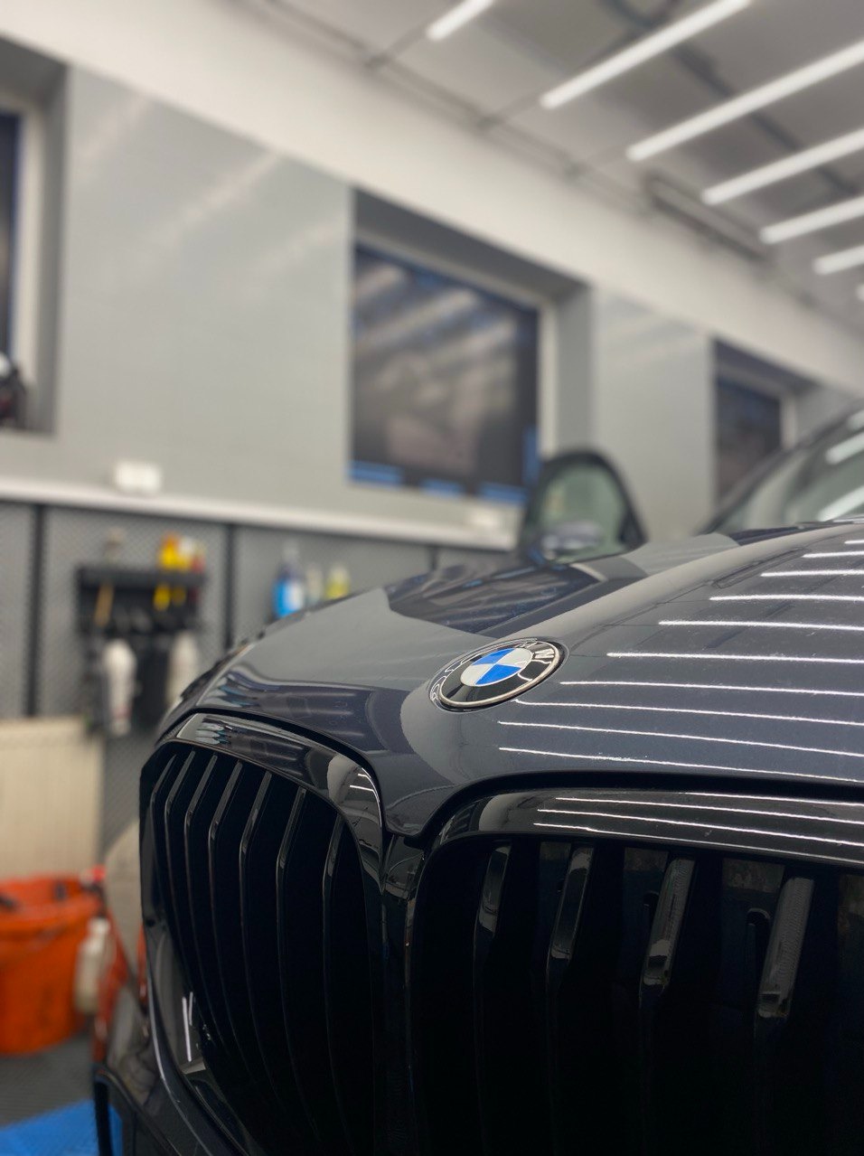 Błyszczący, czarny grill i logo BMW w zbliżeniu, po zabiegach pielęgnacyjnych. Widoczne detale karoserii i oświetlenie warsztatowe.