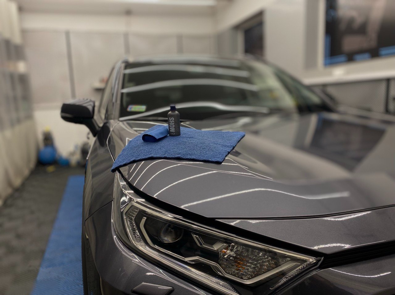 Błyszcząca maska auta z reflektorem, niebieska ściereczka z mikrofibry i butelka produktu do detailingu w studiu pielęgnacji pojazdów.