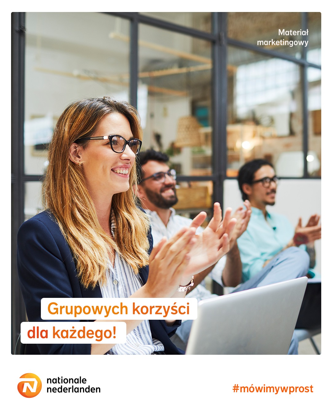 Uśmiechnięta kobieta w okularach klaszcze w dłonie podczas prezentacji, za nią dwóch mężczyzn również klaszcze, laptop na pierwszym planie, logo Nationale Nederlanden w rogu.