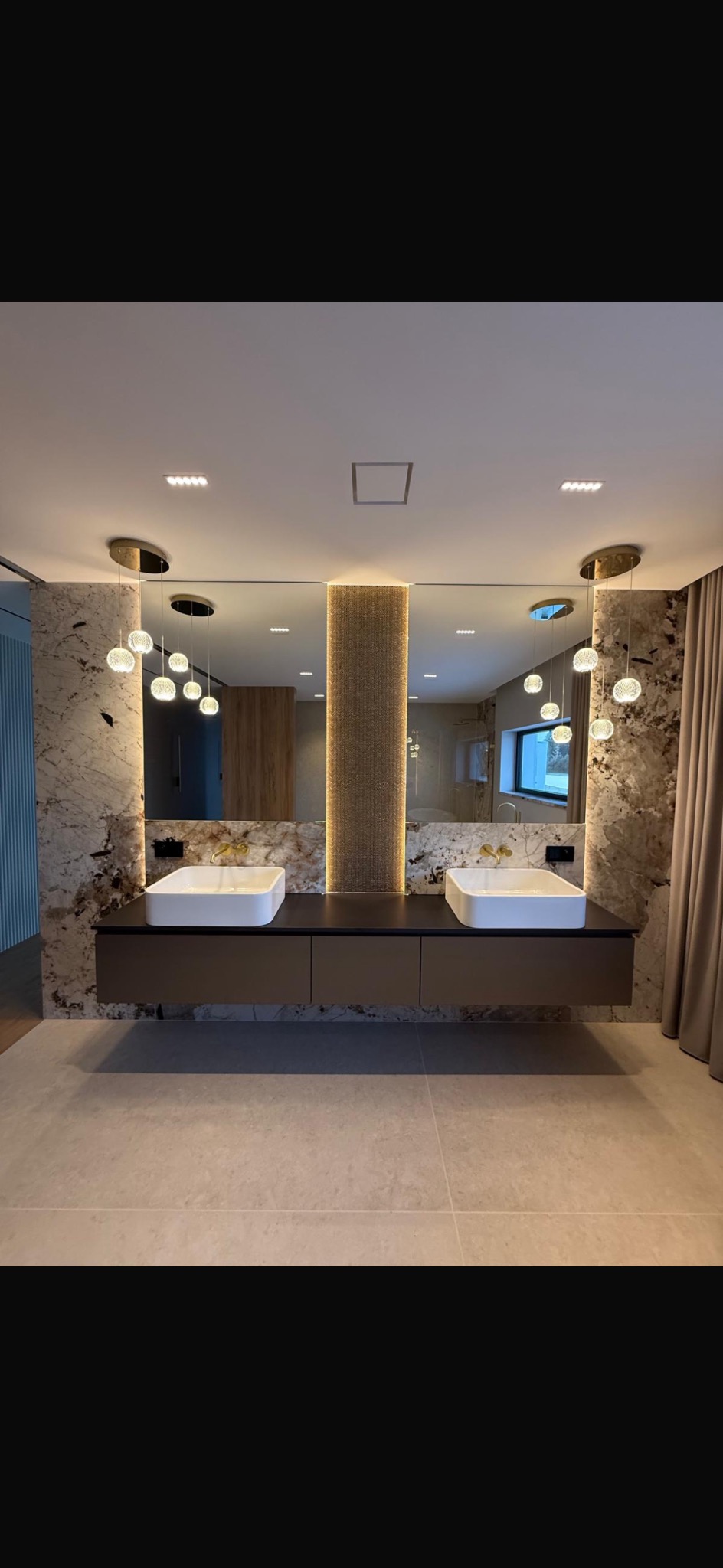 Nowoczesna łazienka z dwoma umywalkami nablatowymi, podświetlanym lustrem i marmurową ścianą. Minimalistyczny design z wiszącą szafką i subtelnym oświetleniem.