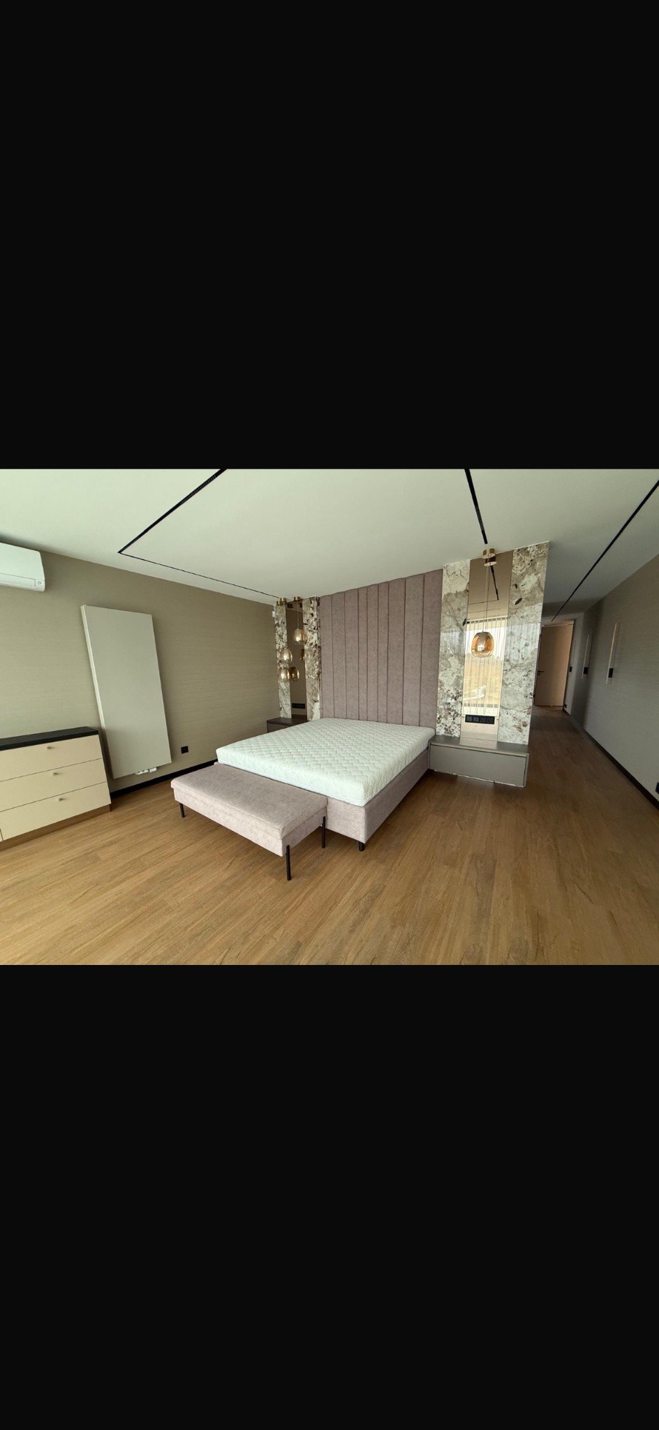 Nowoczesna sypialnia z łóżkiem kontynentalnym, tapicerowanym wezgłowiem i marmurowymi panelami. Parkiet na podłodze, minimalistyczne oświetlenie.