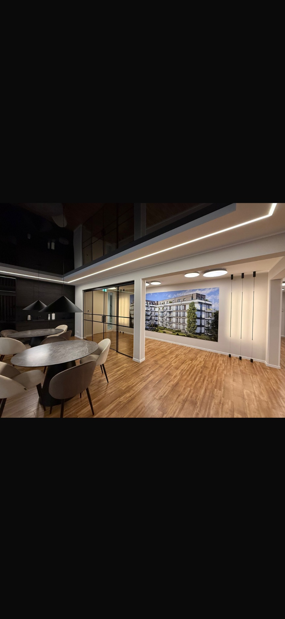 Nowoczesne wnętrze biurowe z drewnianą podłogą, szklanymi drzwiami i fototapetą przedstawiającą budynek mieszkalny. Minimalistyczny design, oświetlenie LED.