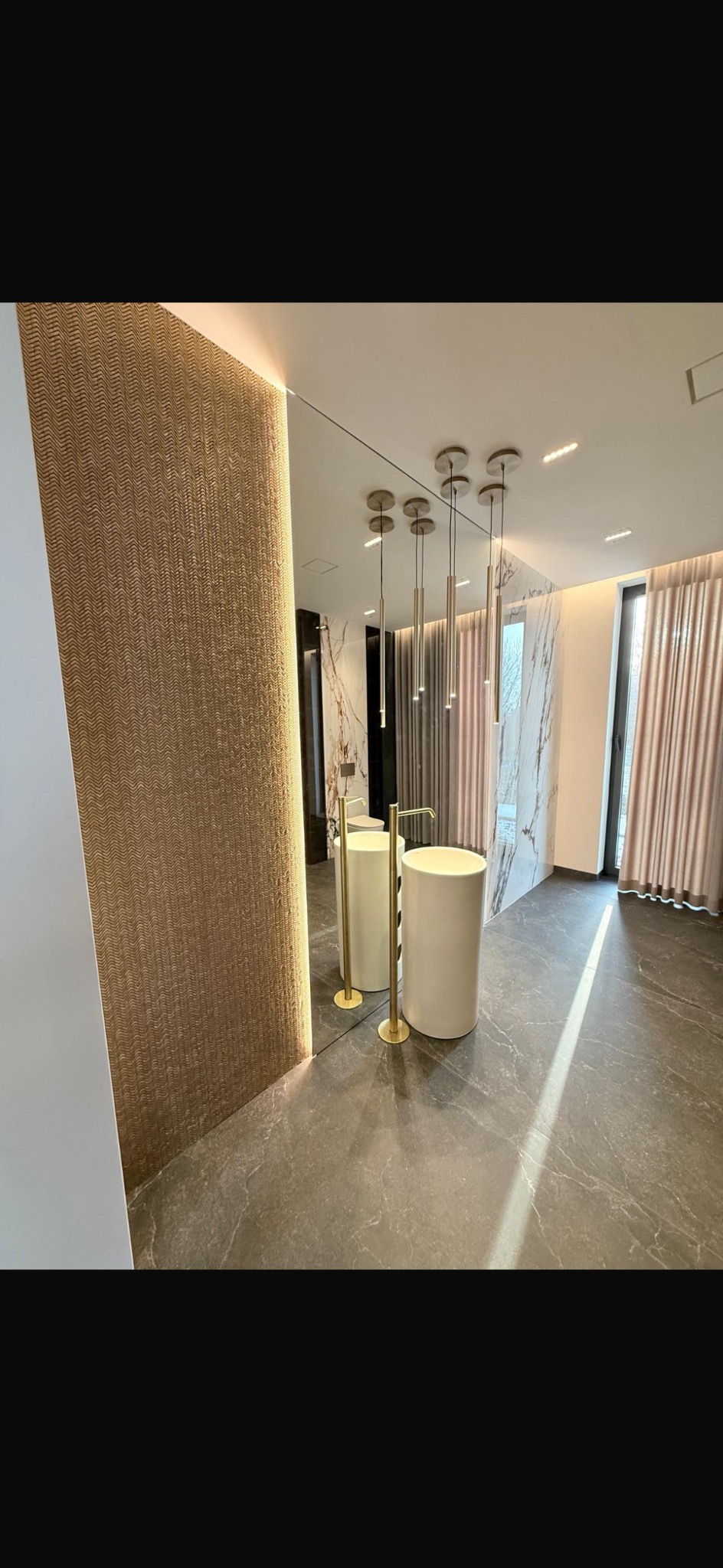 Nowoczesna łazienka z umywalkami cylindrycznymi, złotymi bateriami i lustrem. Dekoracyjna ściana z podświetleniem. Marmurowe wykończenie i designerskie lampy.