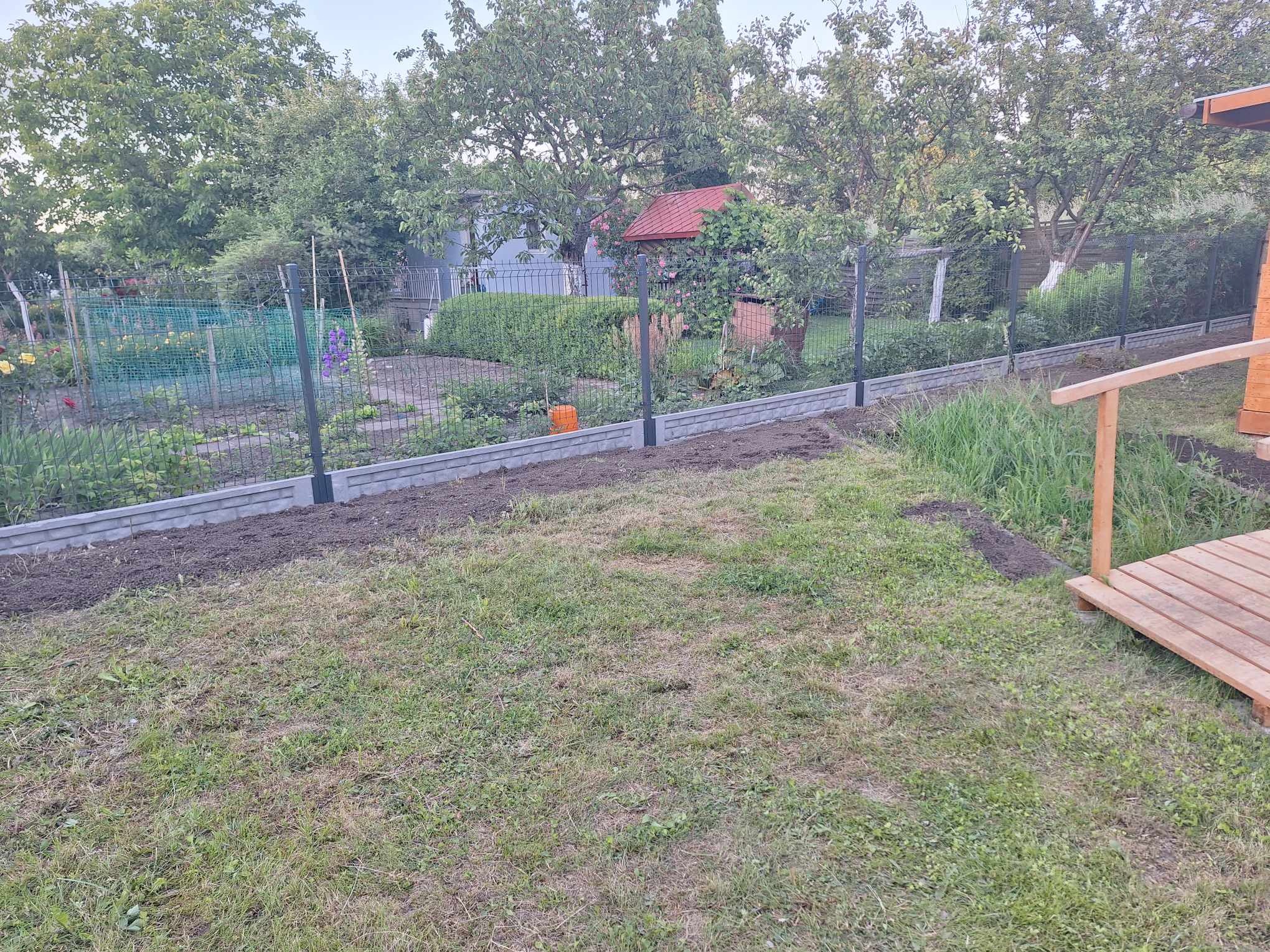 Nowo postawione ogrodzenie panelowe z podmurówką betonową oddzielające ogród od trawnika, widoczne rabaty kwiatowe i drzewa w tle.