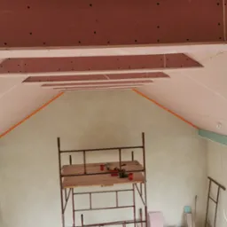 Montaż płyt kartonowo-gipsowych na poddaszu, widoczny ruszt, fragment ocieplenia i narzędzia pracy.