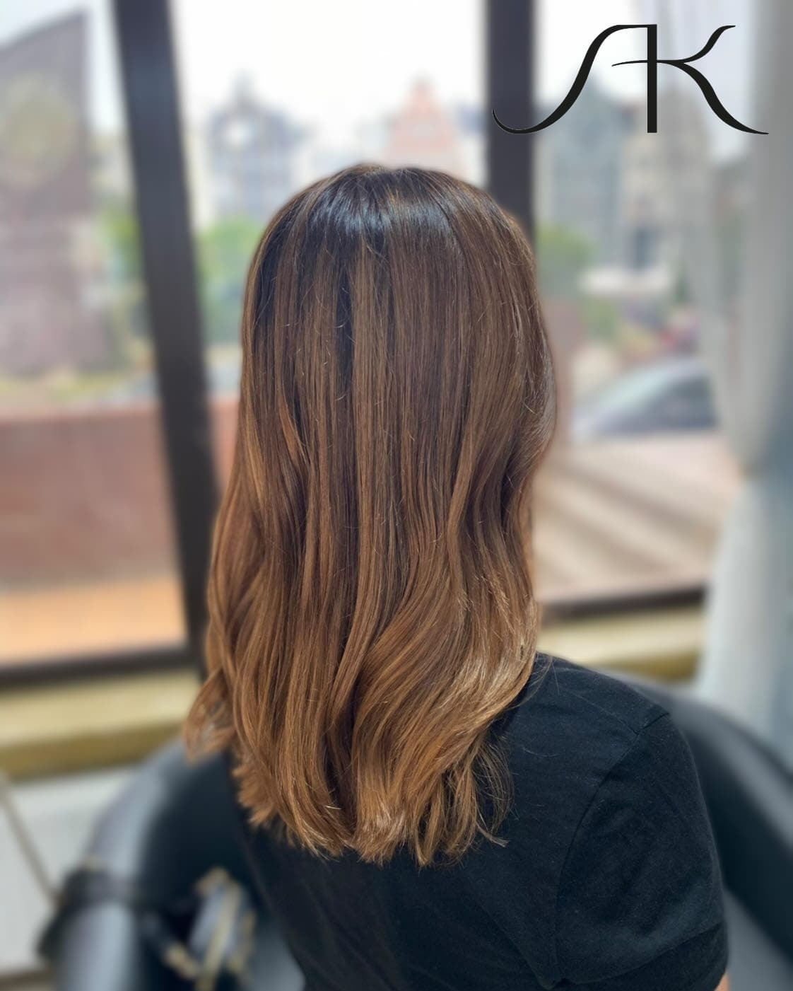 Brązowe włosy z refleksami, delikatne fale, widok z tyłu na tle okna.