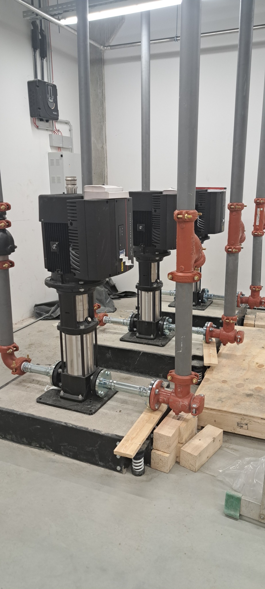 Rząd pionowych pomp przemysłowych, czarne silniki i srebrne korpusy, połączone rurami z czerwonymi zaworami w surowym, betonowym pomieszczeniu.