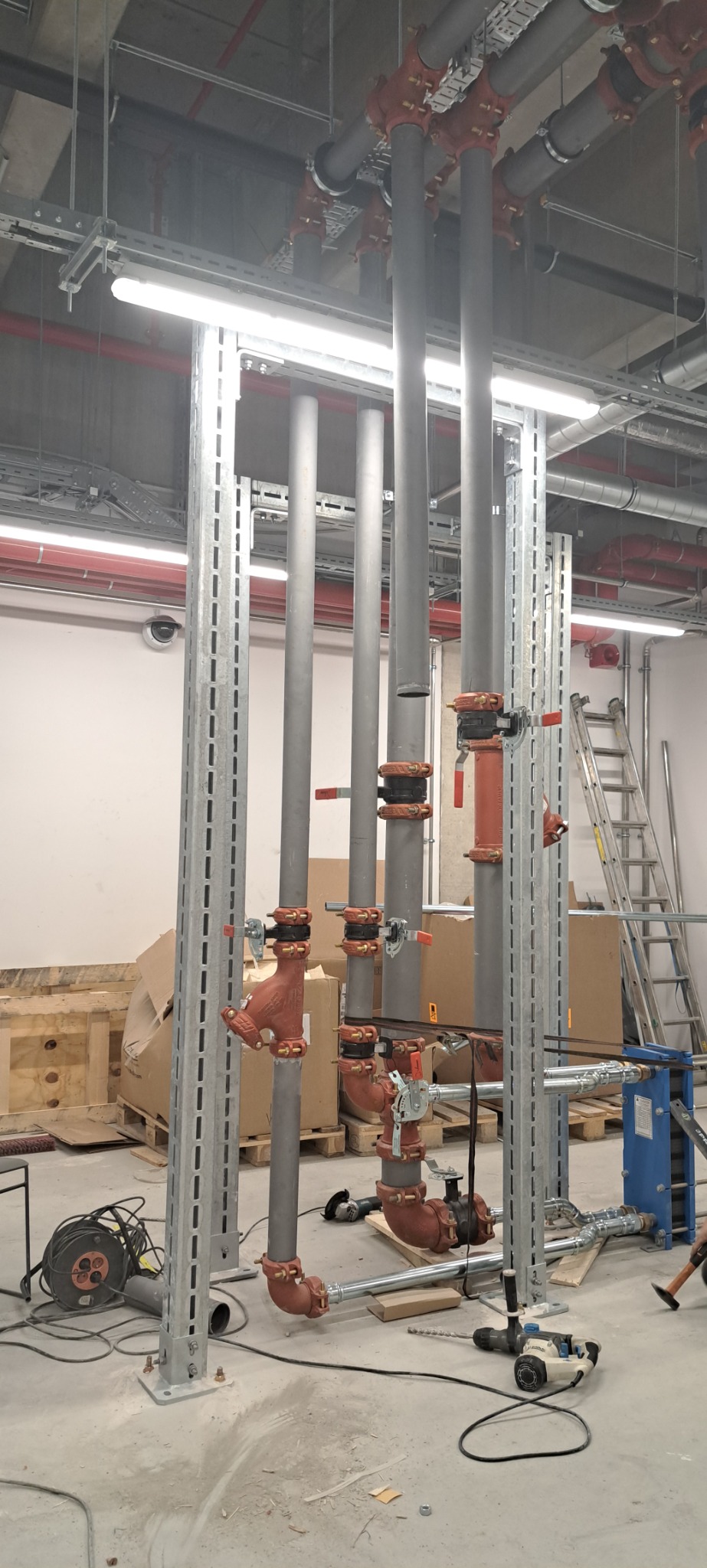 Montaż instalacji przemysłowej w Płocku: rury stalowe, zawory i elementy mocujące w surowym, przemysłowym wnętrzu z widocznymi narzędziami i materiałami budowlanymi.