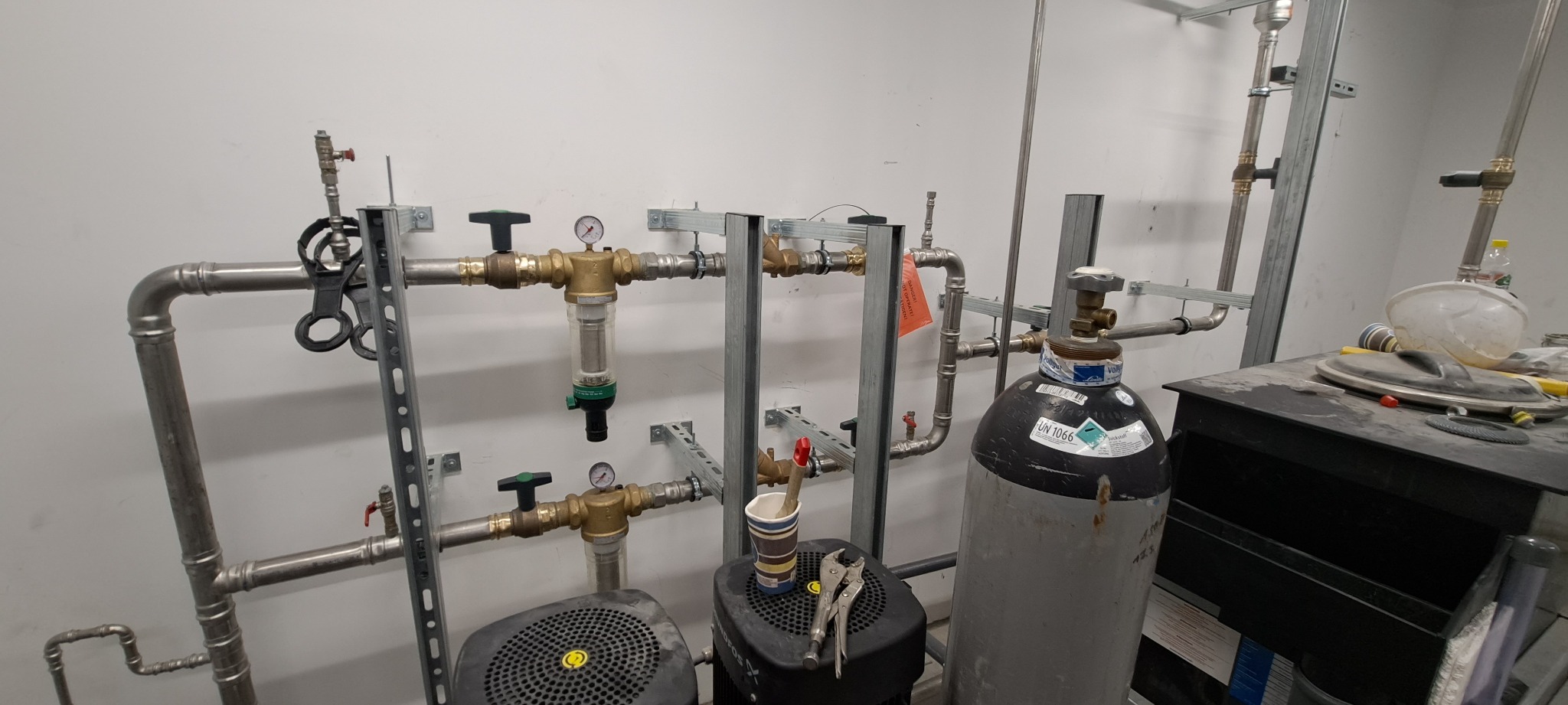 Instalacja przemysłowa z rurami, zaworami, manometrami i butlą gazową, widoczne ślady montażu i narzędzia.