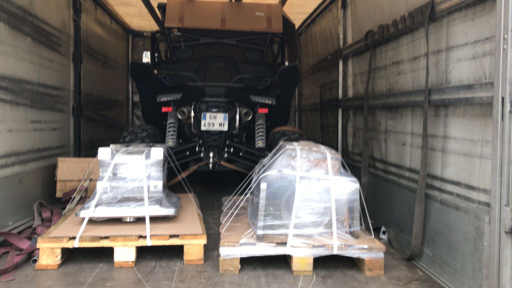 Wnętrze naczepy z załadowanym pojazdem typu buggy z widocznymi tablicami rejestracyjnymi oraz dwiema paletami z zapakowanymi elementami metalowymi, zabezpieczonymi folią stretch.