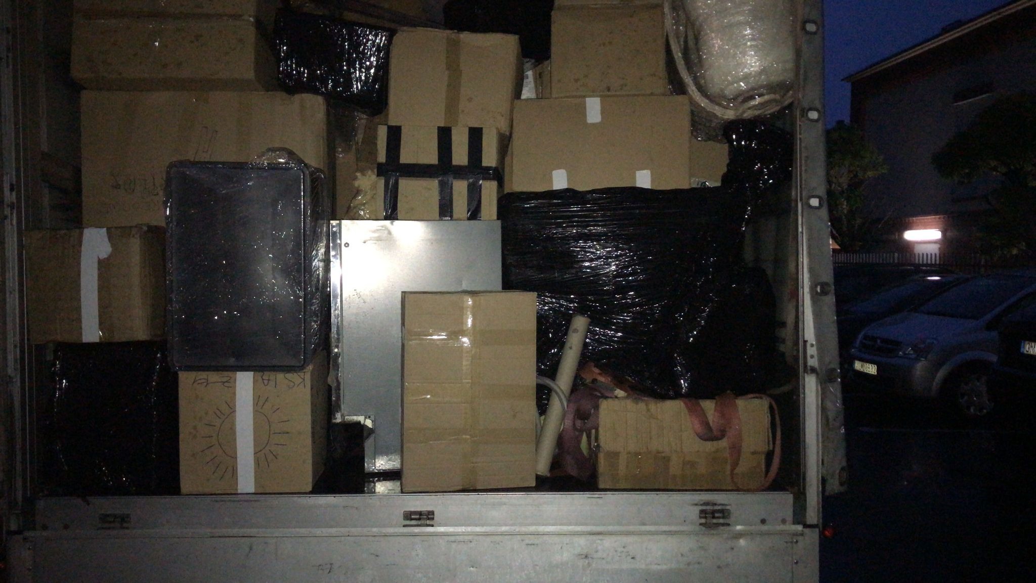 Wnętrze skrzyni ładunkowej wypełnione kartonami, folią stretch i zabezpieczonymi przedmiotami podczas transportu, widoczne elementy mocujące ładunek.