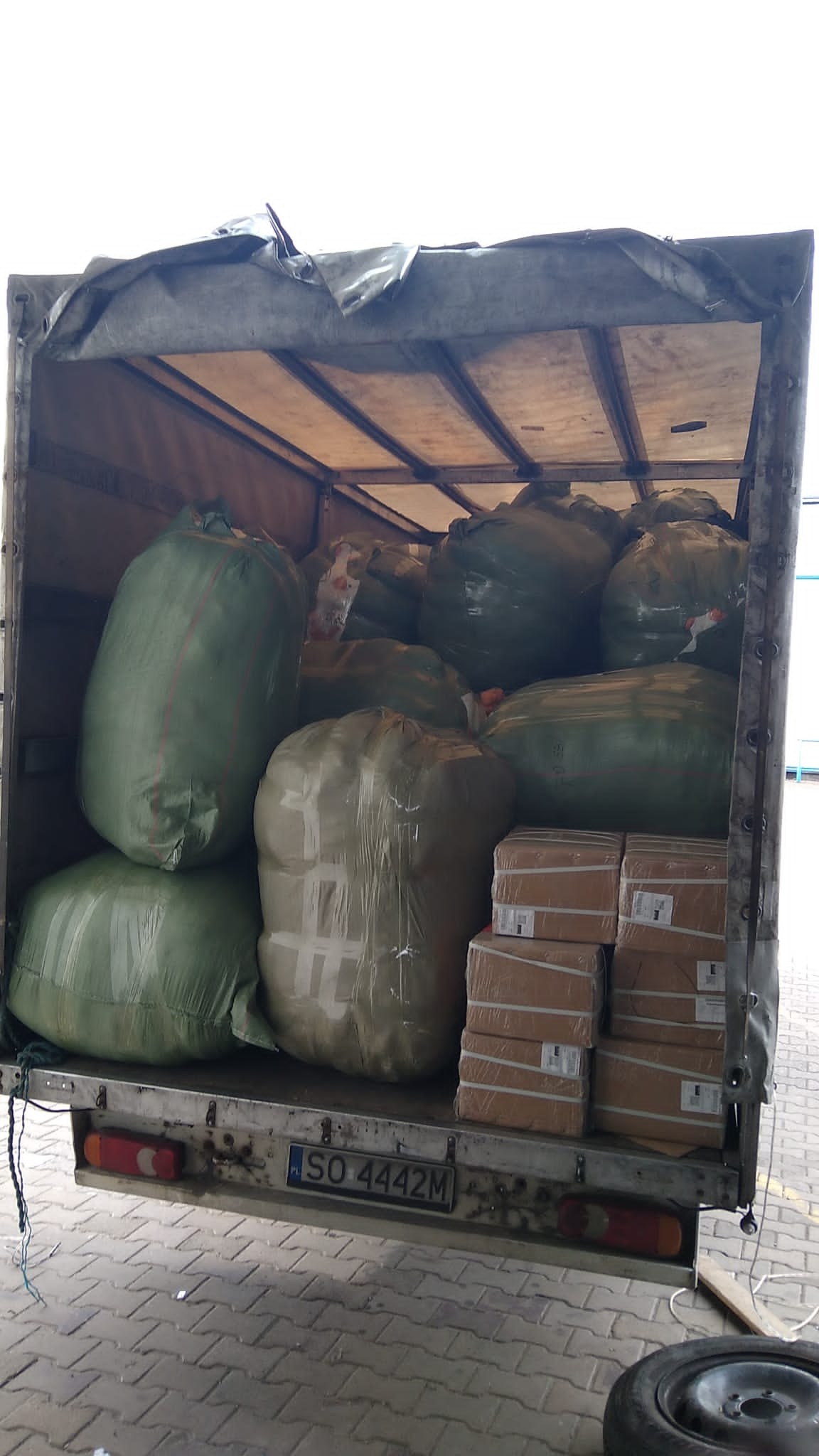 Załadunek busa: worki transportowe i kartony zabezpieczone folią, widoczna tablica rejestracyjna SO 4442M