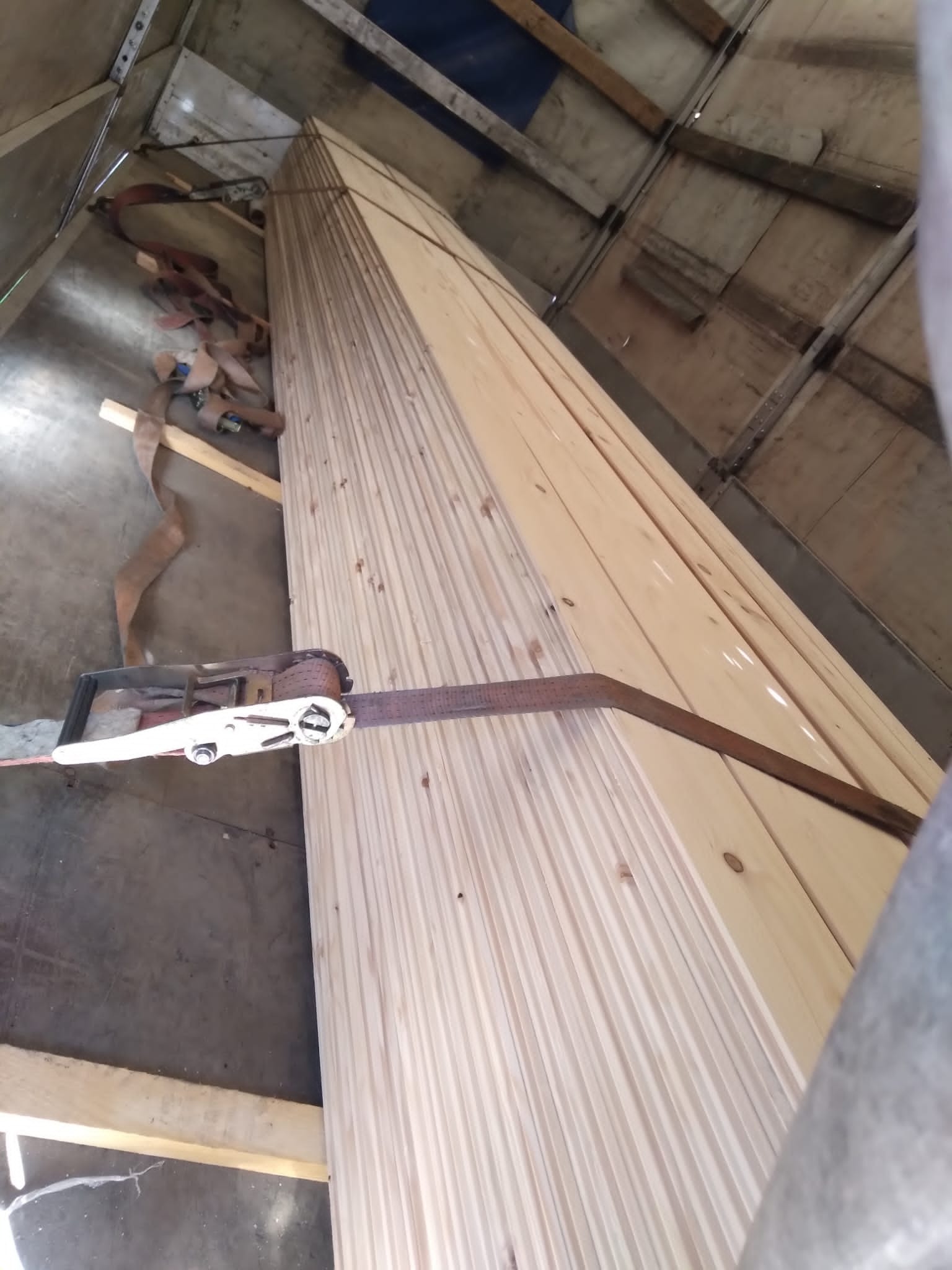 Deski zabezpieczone pasem transportowym wewnątrz pojazdu dostawczego, widok z dołu.