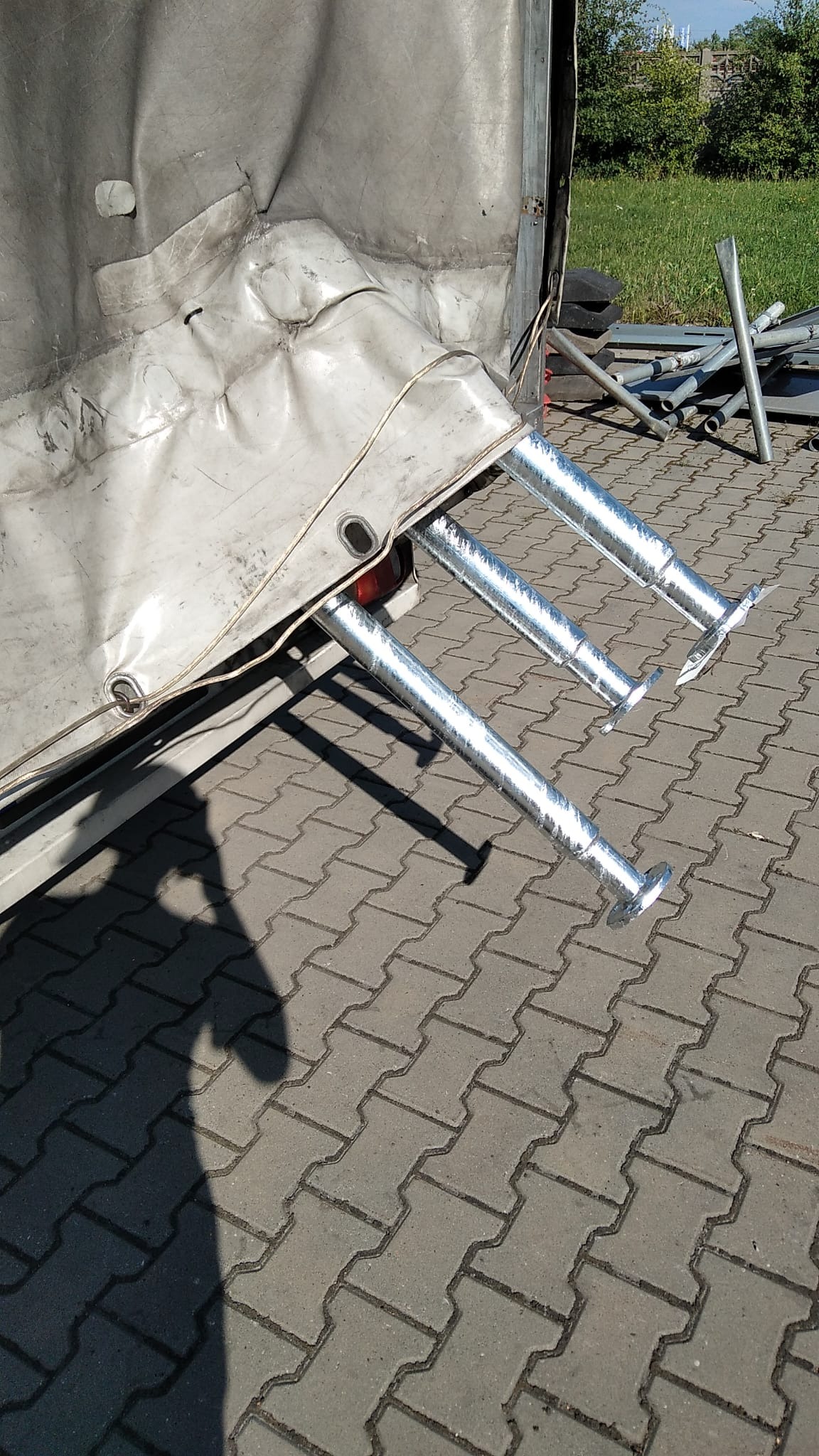 Tylna część brudnej naczepy z rozłożonymi, chromowanymi podporami na brukowanym podłożu.