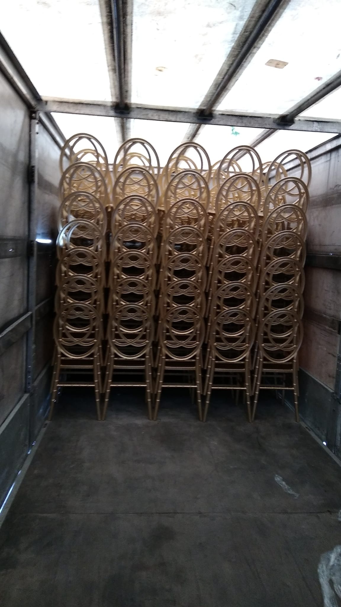 Stos złotych krzeseł Chiavari ułożonych w rzędach wewnątrz przestrzeni ładunkowej busa, widoczne metalowe ściany i sufit pojazdu.