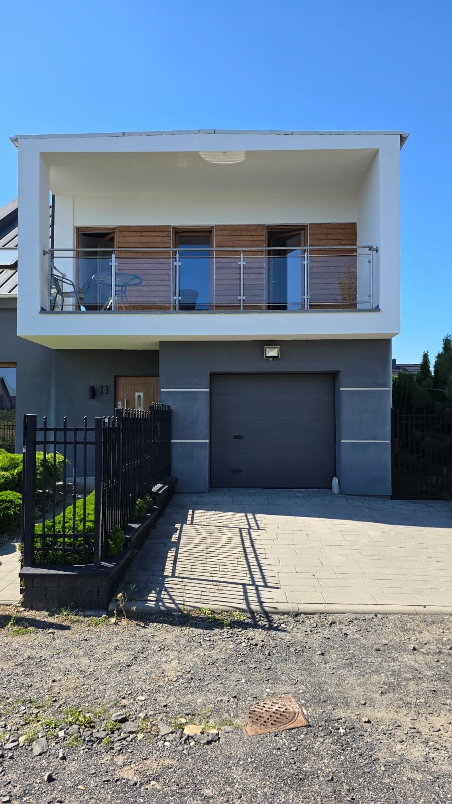 Nowoczesny dom jednorodzinny z balkonem i garażem w szarej kolorystyce, widok z zewnątrz na elewację i podjazd.