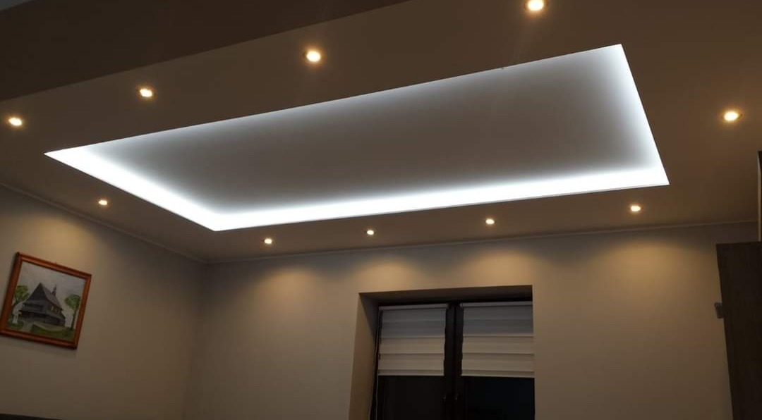 Nowoczesny sufit podwieszany z oświetleniem LED, widoczne halogeny punktowe i obraz na ścianie w tle.