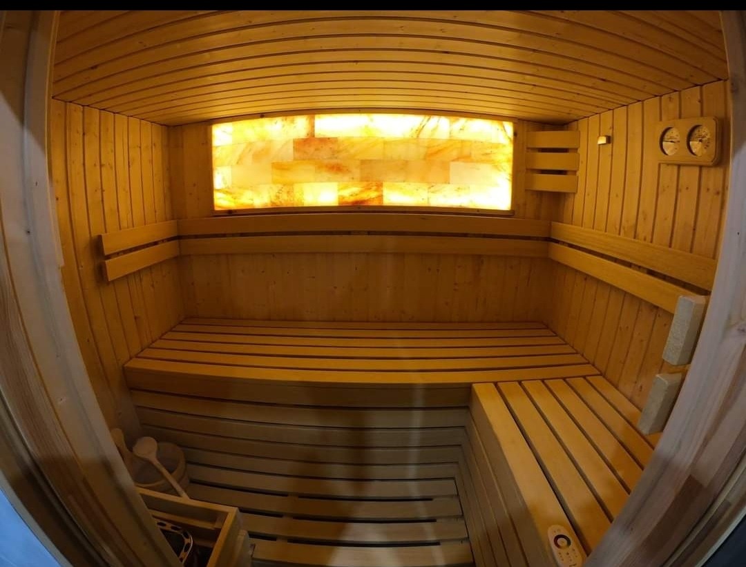Wnętrze drewnianej sauny z oświetlonym panelem solnym, widoczne ławy, akcesoria do sauny i termometr.