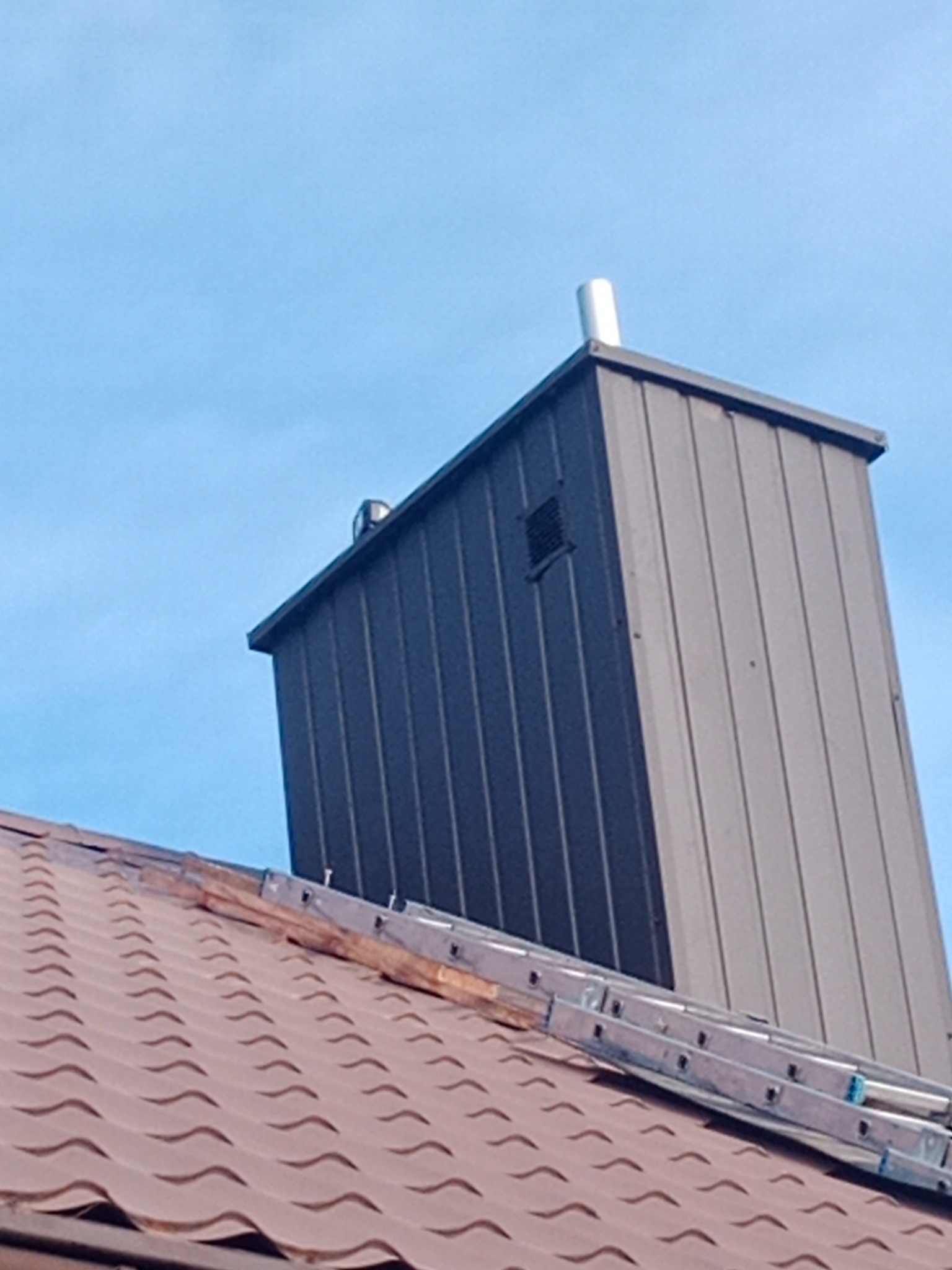 Obróbka blacharska komina na dachu z blachodachówki, widoczna drabina dekarska.