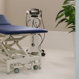 Interfizjo S.A. - Niebieski stół do terapii manualnej z regulacją wysokości, obok białe urządzenie do fizykoterapii marki Chatta, w tle roślina doniczkowa.