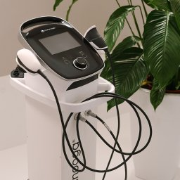 Interfizjo S.A. - Aparat do fizykoterapii marki Chattanooga na białym wózku, z widocznymi głowicami i kablami, na tle zielonej rośliny doniczkowej.