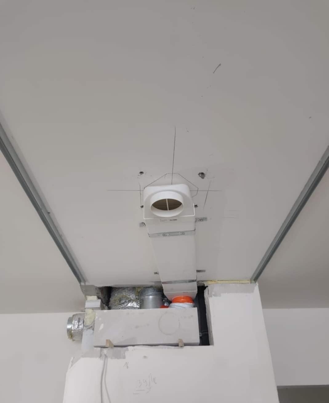 Montaż systemu wentylacji pod sufitem podwieszanym z płyt karton-gips. Widoczne białe rury i elementy instalacji. Prace wykończeniowe w toku.