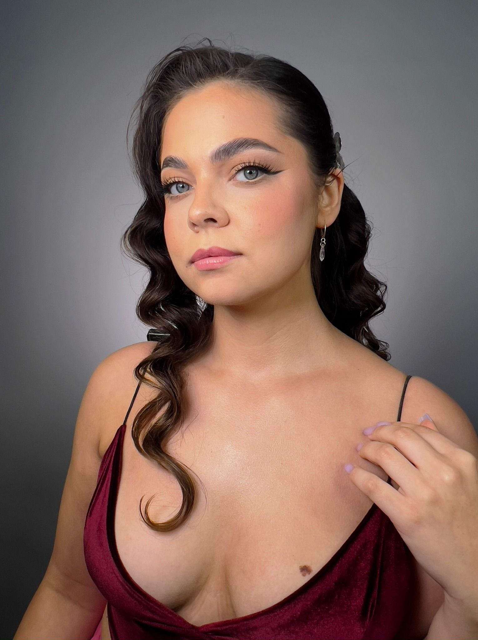 Portret kobiety z profesjonalnym makijażem: wyraźne kreski, podkreślone brwi, delikatny róż na policzkach, błyszczące usta i elegancka fryzura z upięciem.