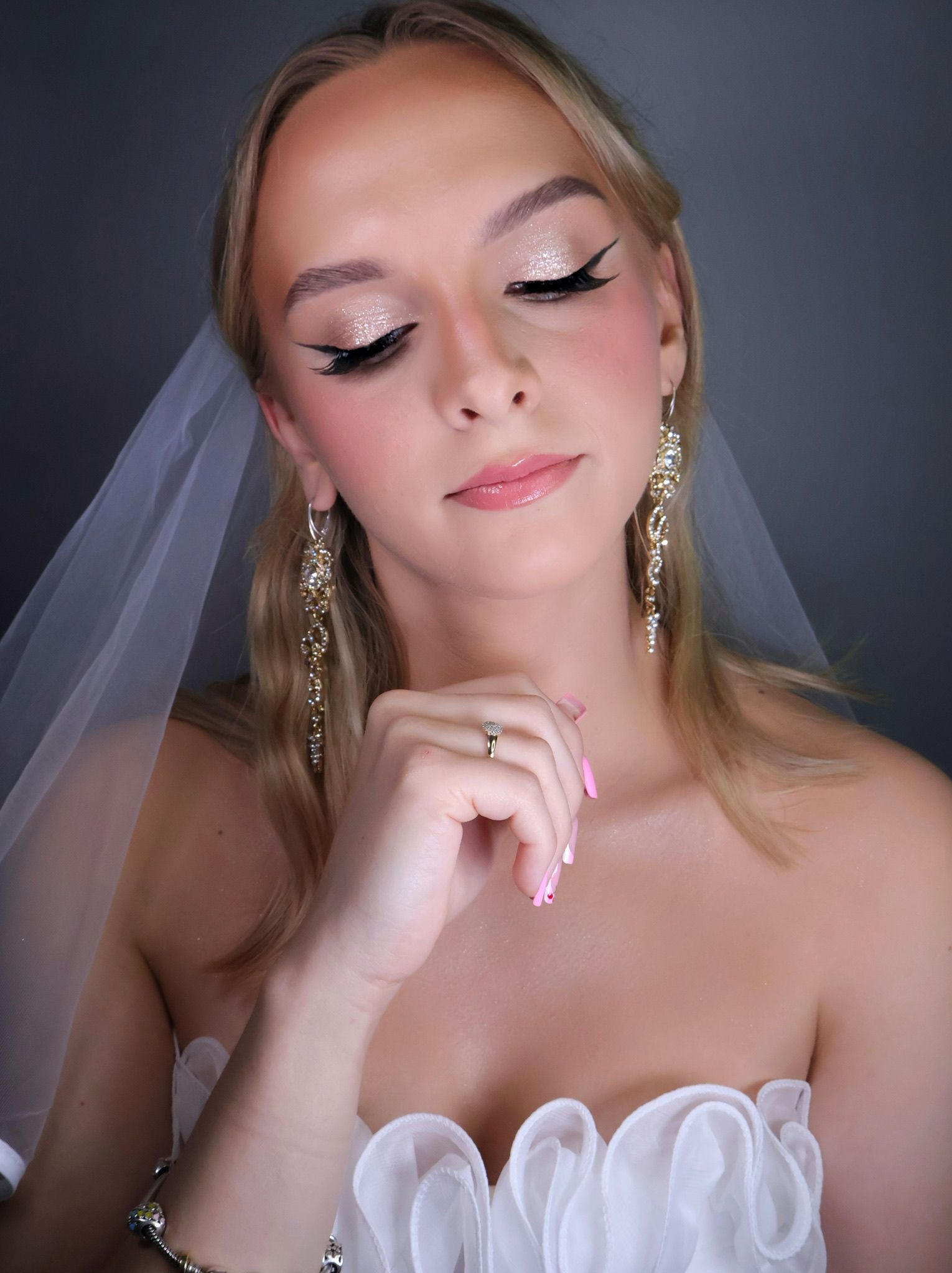 Panna młoda z subtelnym makijażem ślubnym: błyszczące powieki, czarna kreska, róż na policzkach i delikatny błyszczyk. Uwagę przyciągają długie, złote kolczyki.