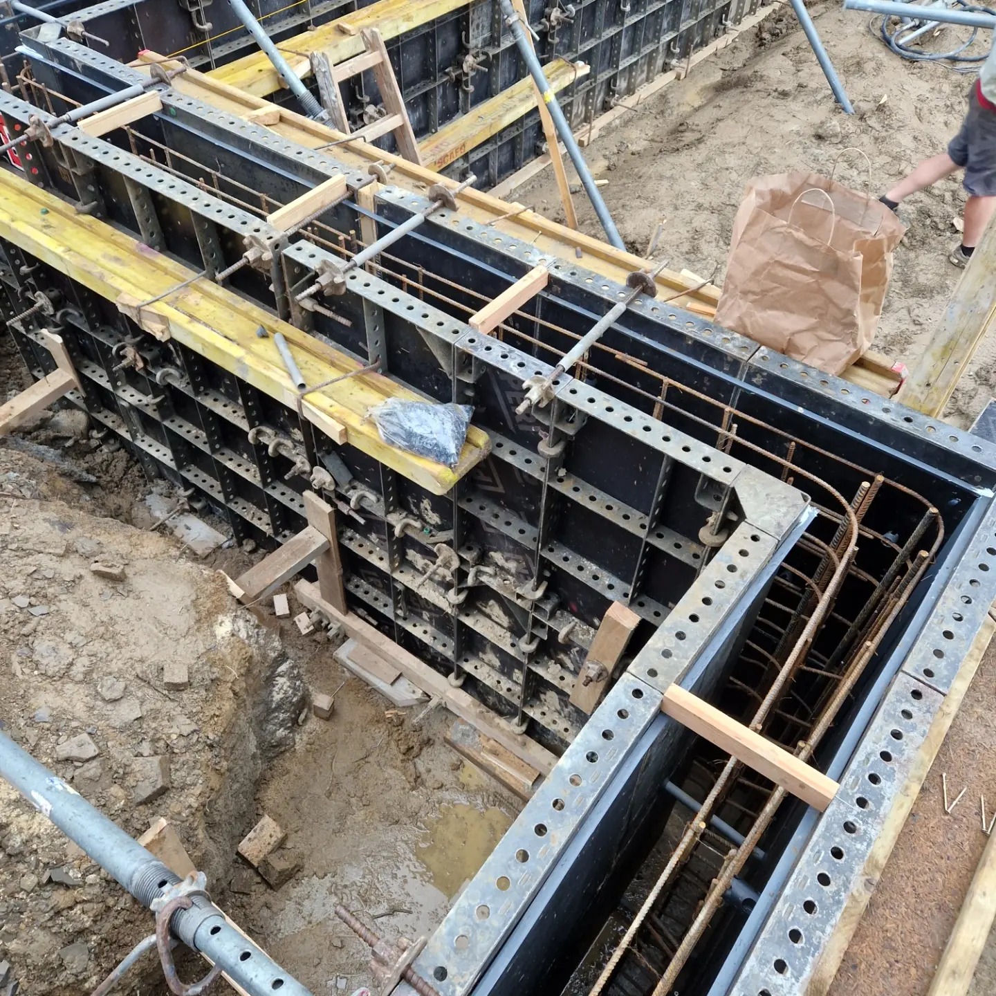 Zbrojenie w szalunkach, przygotowane do zalania betonem, widoczne elementy konstrukcyjne i pręty zbrojeniowe, na górze leży papierowa torba.