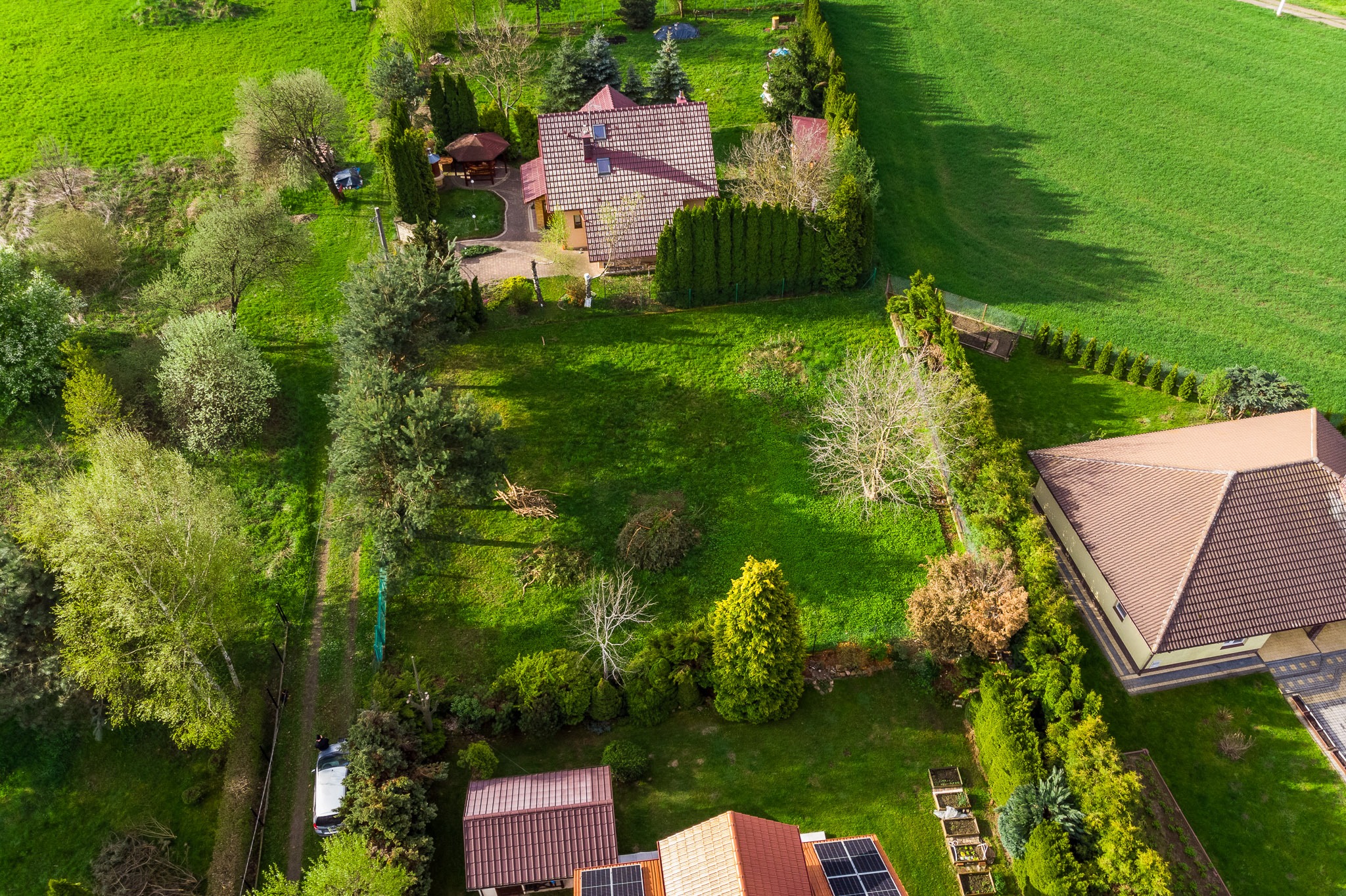 Widok z lotu ptaka na zadbane osiedle domów jednorodzinnych z zielonymi trawnikami i drzewami, niektóre domy posiadają panele słoneczne na dachu.
