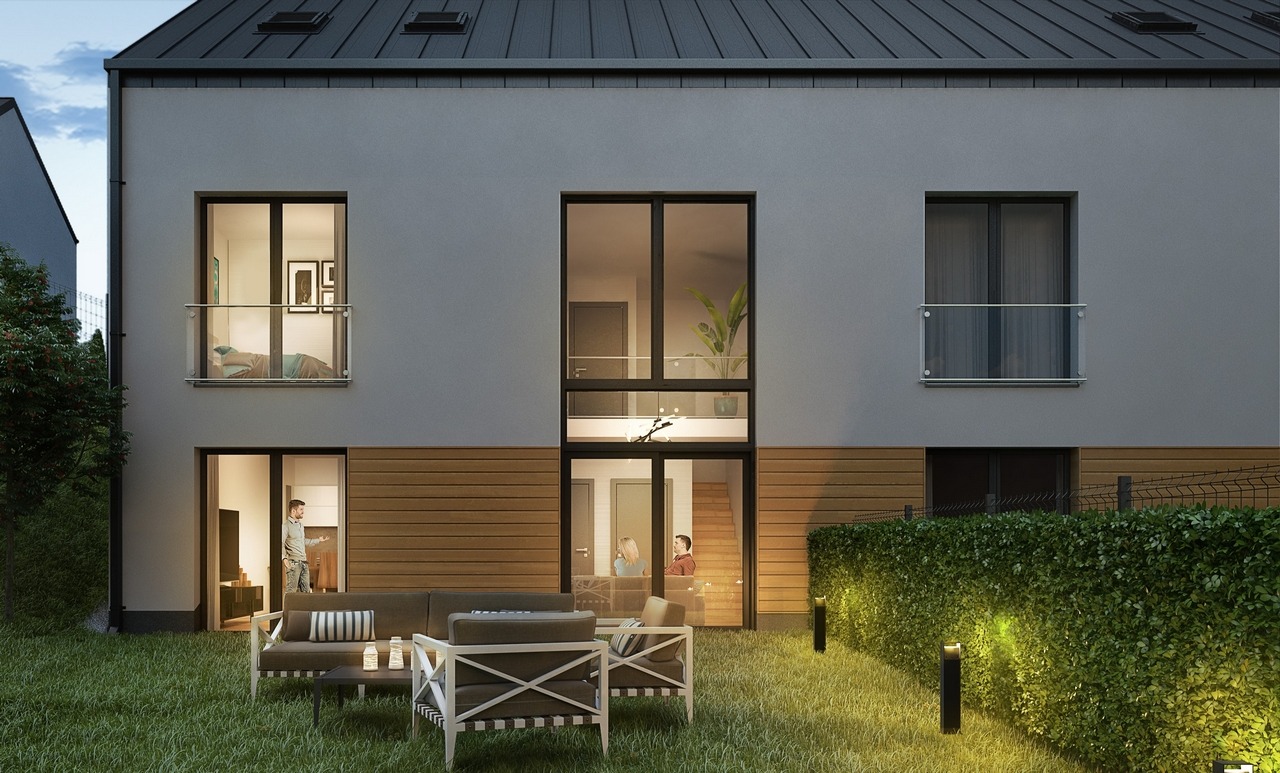 Dwupiętrowy dom z szarego tynku z drewnianą elewacją na parterze i oknami balkonowymi, z widocznym wnętrzem, oświetlonym trawnikiem i zestawem mebli ogrodowych.