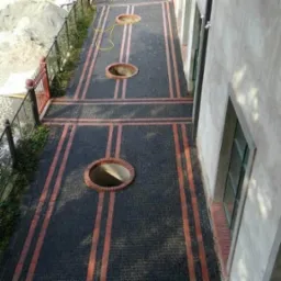 Wykończone podwórko z ciemnej kostki brukowej z ceglanymi pasami i okrągłymi otworami z ceglanym obramowaniem, widok z góry.