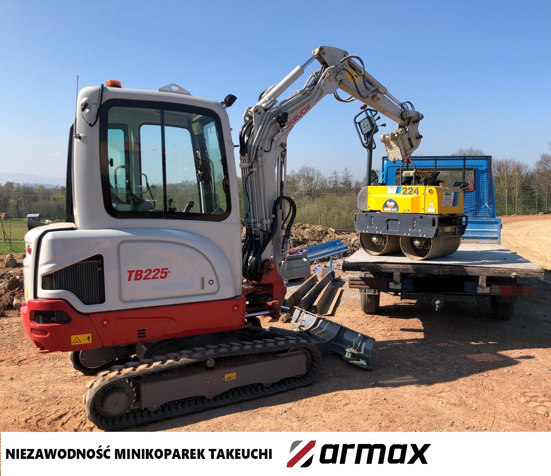 Szara minikoparka Takeuchi TB225 podnosi żółty walec wibracyjny na przyczepę samochodu ciężarowego na placu budowy.