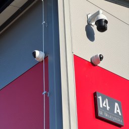 ITCAM Rafał Iwańczyk - Dwie kamery kopułkowe i jedna obrotowa PTZ zamontowane na elewacji budynku o szaro-czerwonej kolorystyce, widoczny adres budynku na tabliczce.