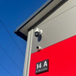 Dwie kamery monitoringu zamontowane na elewacji budynku z numerem adresowym 14A Ul. Olsztyńska, na tle błękitnego nieba.
