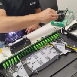 Technik łączy światłowody w skrzynce rozdzielczej za pomocą spawarki światłowodowej, widoczne narzędzia i elementy złączne.