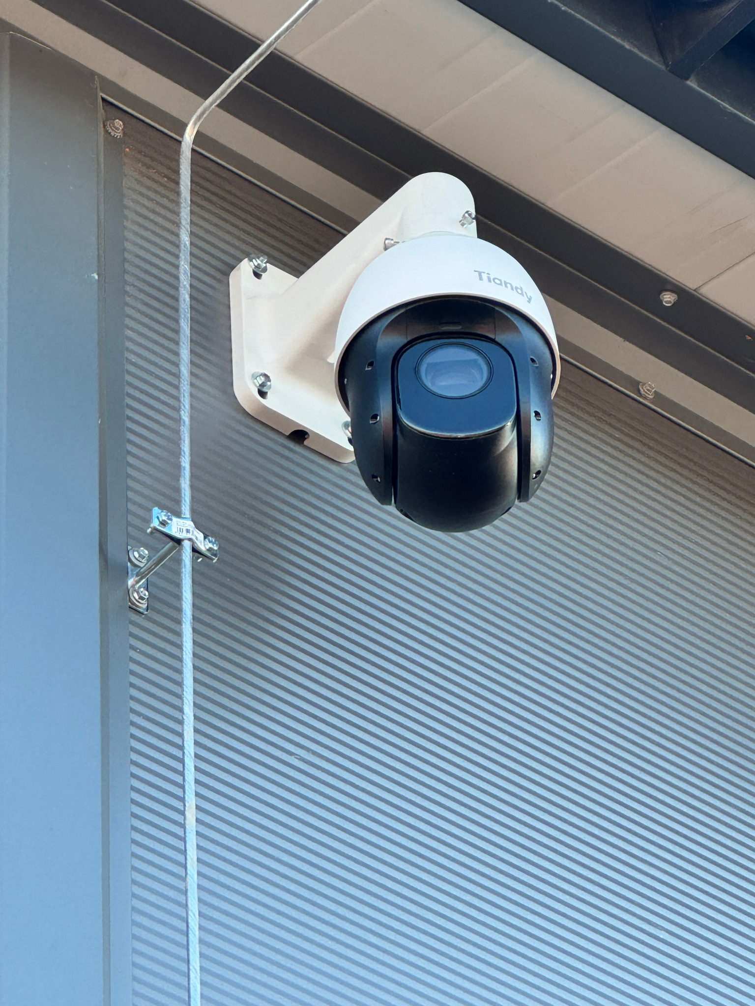Zewnętrzna kamera obrotowa Tiandy, zamontowana na ścianie z blachy trapezowej, zabezpieczona kablem w metalowej rurce.