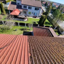 Czyszczenie dachówki z mchu za pomocą myjki ciśnieniowej, widoczny kontrast między oczyszczoną a porośniętą mchem częścią dachu.