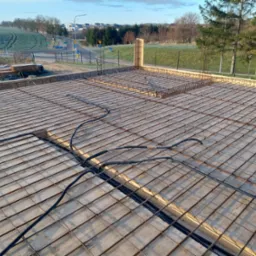 Zbrojenie stropu z ułożonymi przewodami instalacji elektrycznej, widok z góry na budowę domu, w tle krajobraz podmiejski.