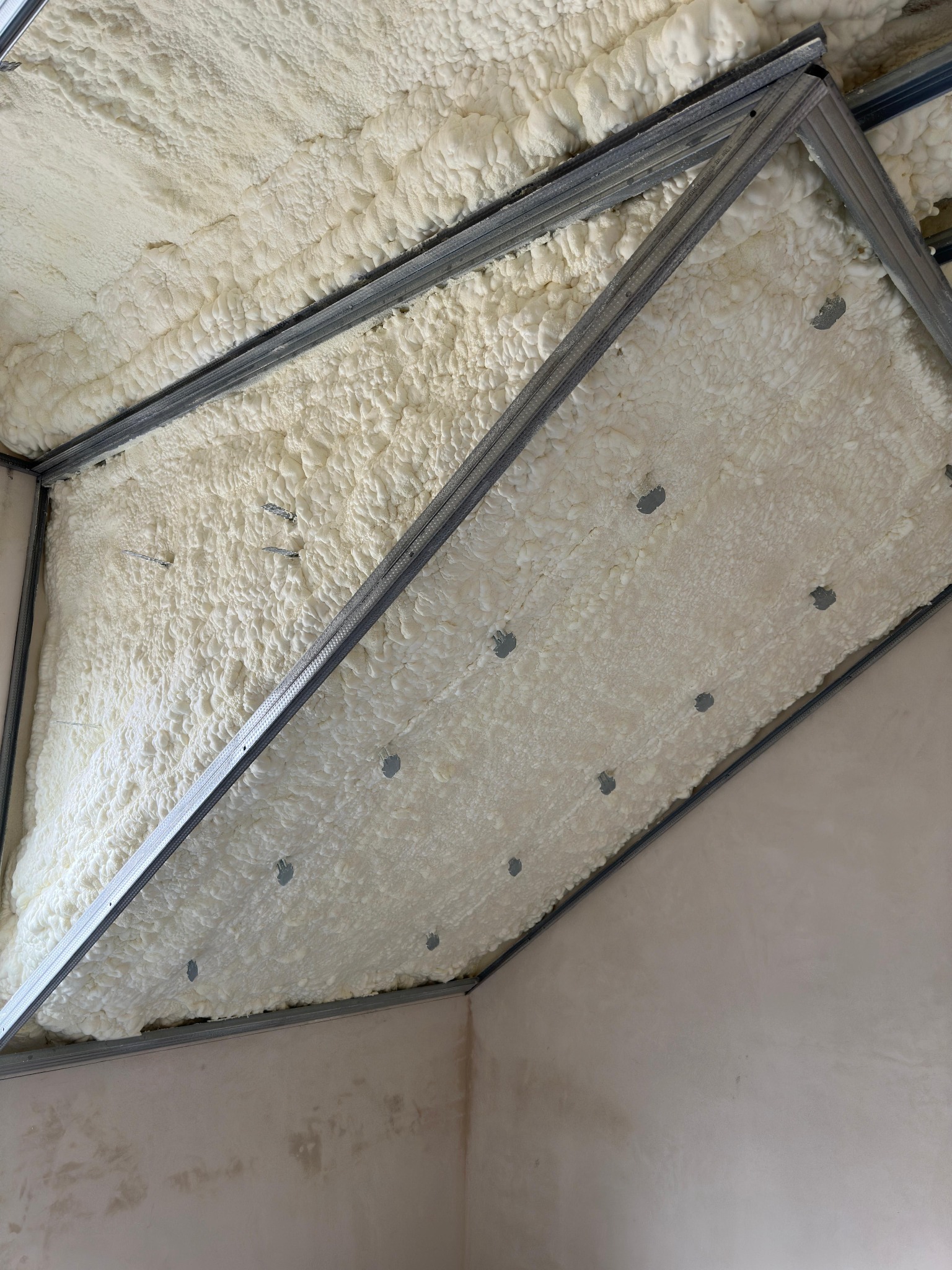 Natrysk pianki poliuretanowej na stropie, widoczne metalowe profile konstrukcyjne i ślady po mocowaniu.