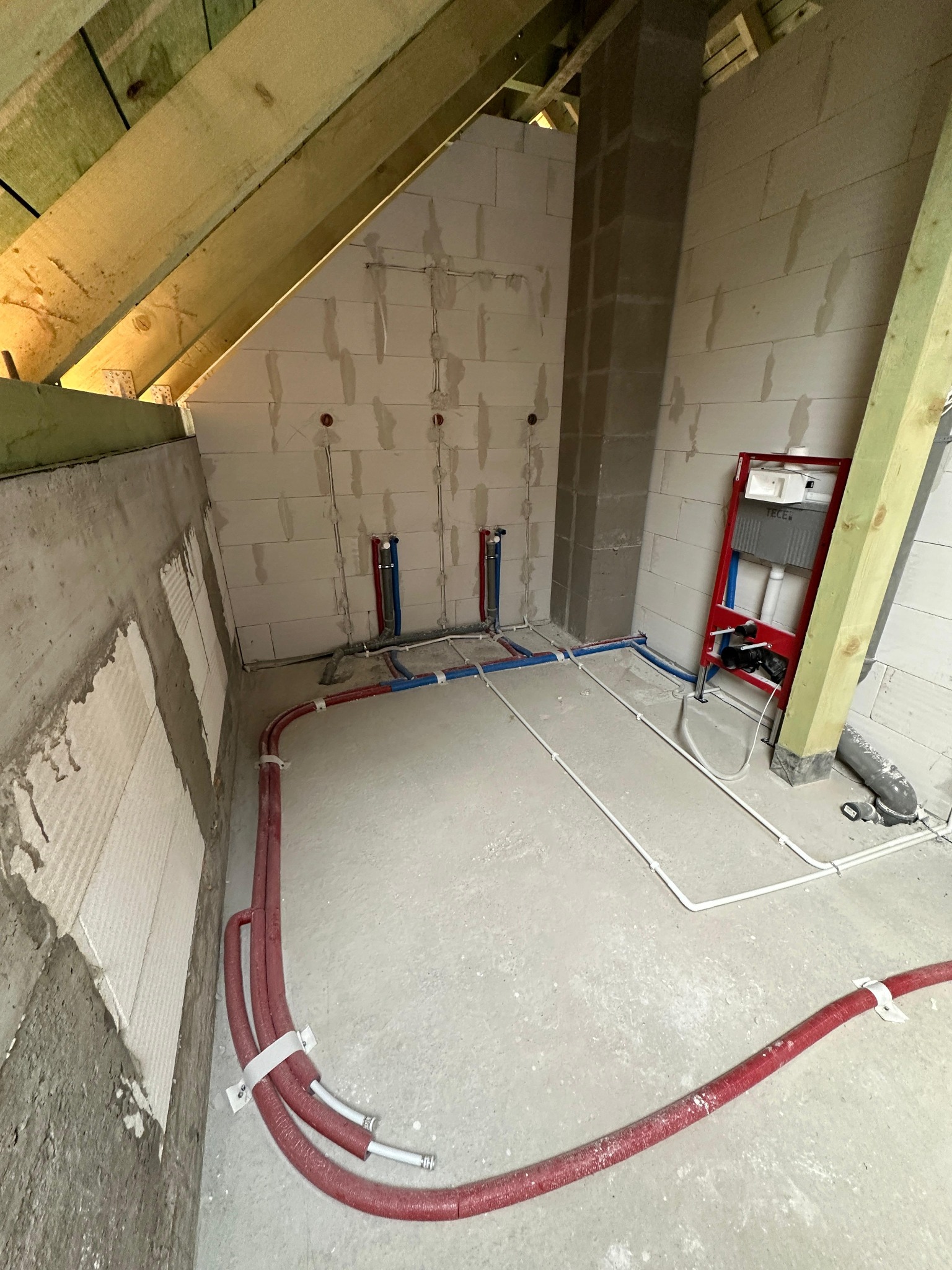 Poddasze w trakcie wykańczania: widoczne rury instalacji wodnej w izolacji, elementy stelaża podtynkowego WC, oraz pion kanalizacyjny w surowym stanie.