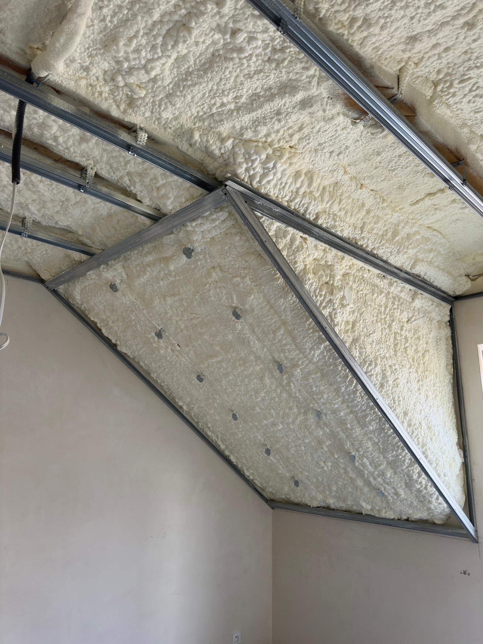 Poddasze z widoczną konstrukcją metalową i natryskiwaną pianą izolacyjną, sufit w trakcie ocieplania.